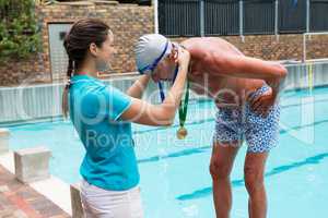 Female coach giving gold medal to senior man