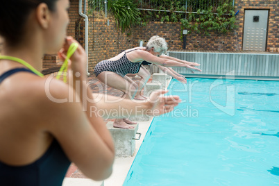 Female trainer whistling while senior women diving into pool
