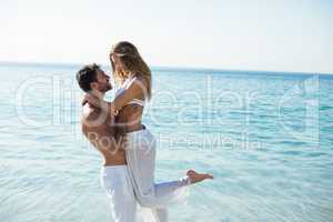 Man carrying girlfriend while standing on shore