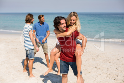 Man piggybacking girlfriend by friends at beach