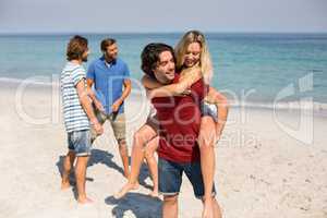 Man piggybacking girlfriend by friends at beach