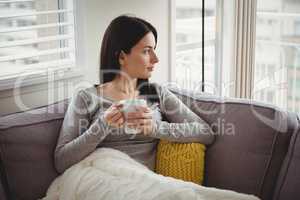Woman holding cup while looking through window