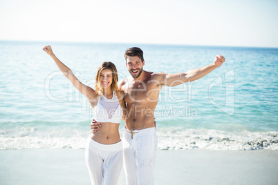 Couple standing with arms outstretched on shore at beach