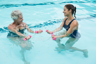 Female coach assisting senior woman in lifting dumbbells