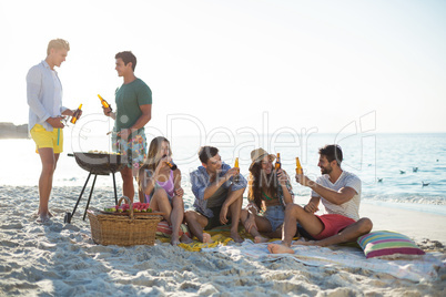 Friends having drinks by barbecue at beach against sky