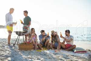 Friends having drinks by barbecue at beach against sky