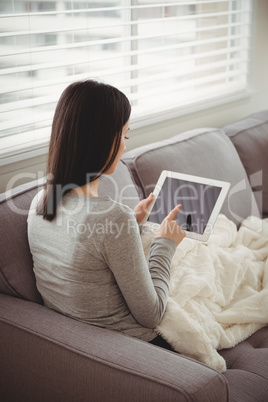 Rear view of woman using tablet while sitting on sofa