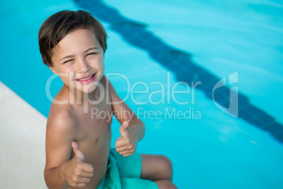 Smiling boy showing thumbs up at poolside