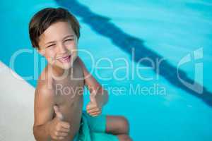 Smiling boy showing thumbs up at poolside