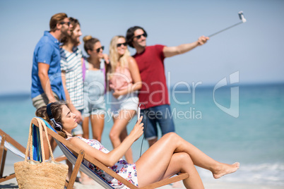 Woman relaxing on deck chair while friends taking selfie