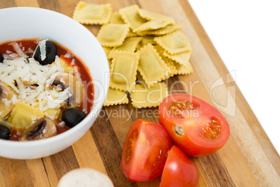Close up of food in bowl by ravioli and vegetables on cutting board