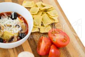 Close up of food in bowl by ravioli and vegetables on cutting board