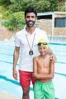 Smiling boy standing with his coach near poolside