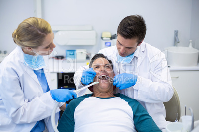 Dentists examining a male patient with tools