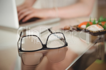 Eyeglasses on table against woman using laptop