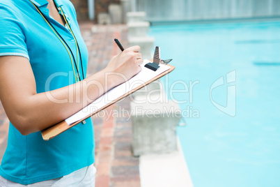 Female coach writing on clipboard near poolside