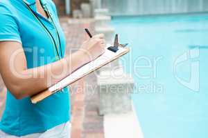 Female coach writing on clipboard near poolside