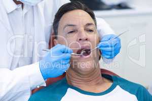 Dentist examining a male patient with tools