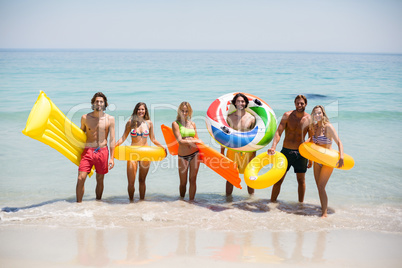 Friends with inflatable rings and pool rafts on seashore