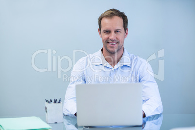 Portrait of smiling dentist working on laptop