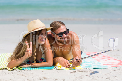 Couple taking selfie with monopod while lying at beach