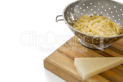 Close up of spaghetti in colander by cheese on cutting board