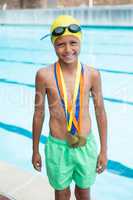Boy with gold medals around his neck standing near poolside