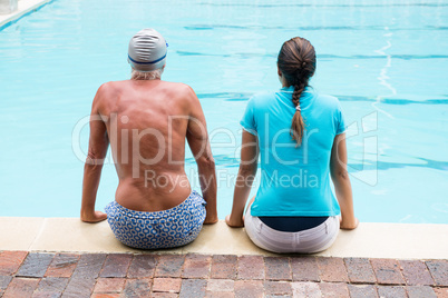 Female coach and senior man sitting at poolside Female coach and senior man sitting at poolside