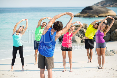 Friends in sportswear stretching while standing on shore