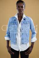 Androgynous man in denim jacket posing against beige background