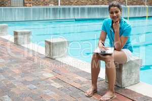 Smiling female coach sitting near poolside