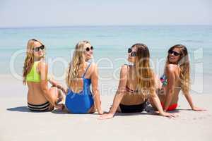 Female friends in bikini relaxing at beach during sunny day