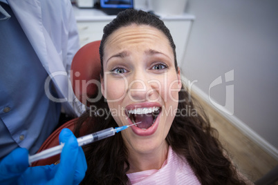 Dentist injecting anesthetics in scared female patient mouth