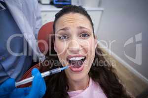 Dentist injecting anesthetics in scared female patient mouth