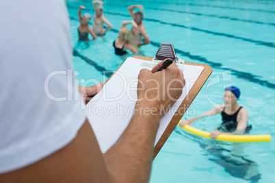 Swim coach writing on clipboard near poolside