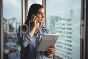 Woman talking on mobile while holding tablet