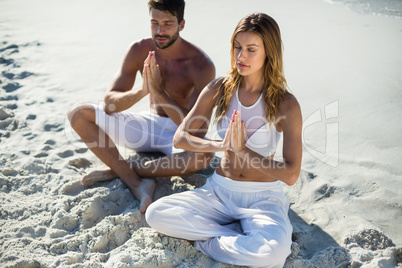 Couple meditating while sitting at beach