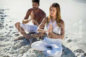 Couple meditating while sitting at beach