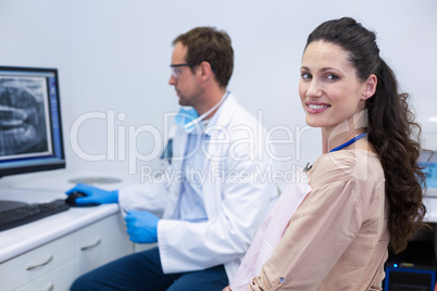 Female patient smiling at camera while dentist looking at an x-ray