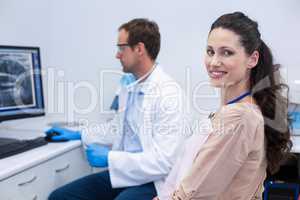 Female patient smiling at camera while dentist looking at an x-ray