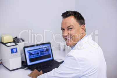 Portrait of happy dentist examining x-ray report on laptop