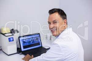 Portrait of happy dentist examining x-ray report on laptop