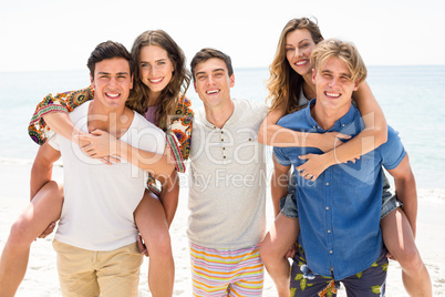Happy men piggybacking women at beach