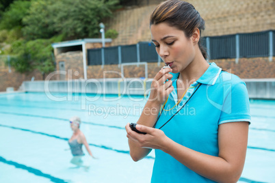 Female coach blowing whistle and looking at stopwatch