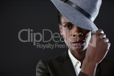 Androgynous man with hand on hat against grey background