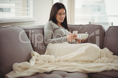 Woman using mobile phone while eating breakfast