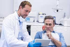 Dentist discussing over digital tablet with male patient