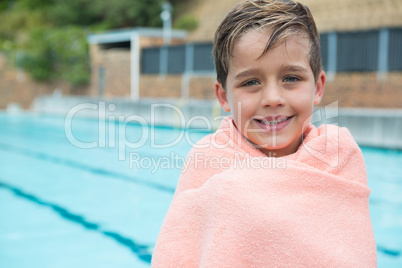 Young boy wrapped in towel standing at poolside