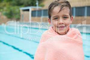 Young boy wrapped in towel standing at poolside