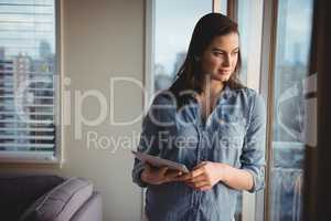 Woman holding digital tablet while looking through window